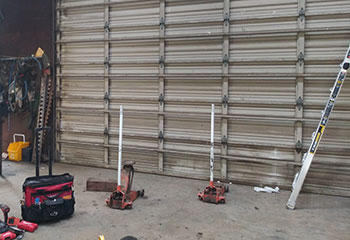 Shop floor with technician tools, jacks, and an old commercial sectional garage door undergoing maintenance in Roseville, CA.