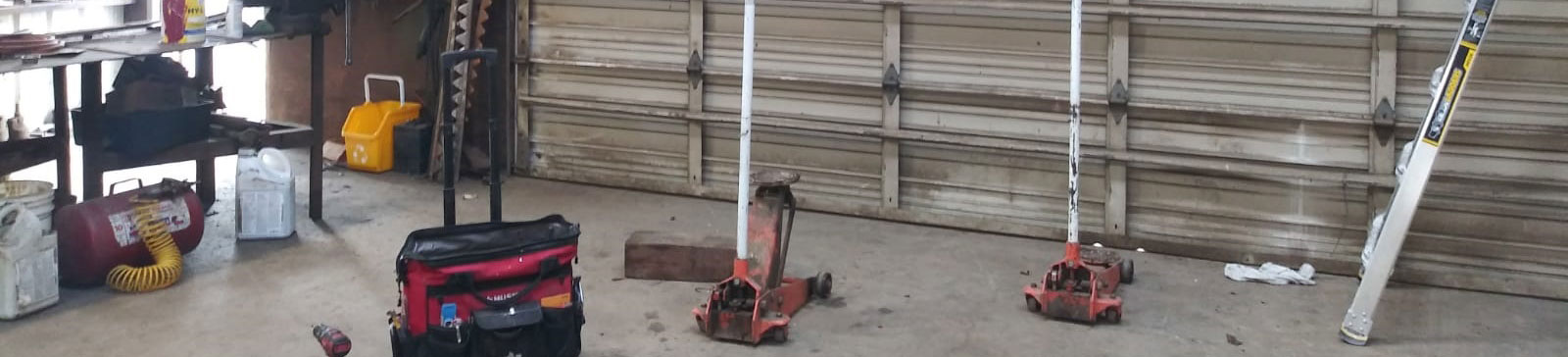 Shop floor with technician tools, jacks, and an old commercial sectional garage door undergoing maintenance in Roseville, CA.